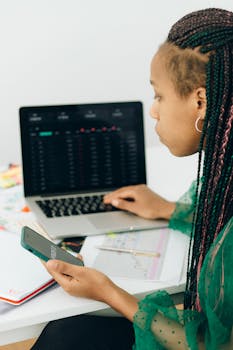 Focused woman working with financial data of Fiverr on laptop and smartphone 
