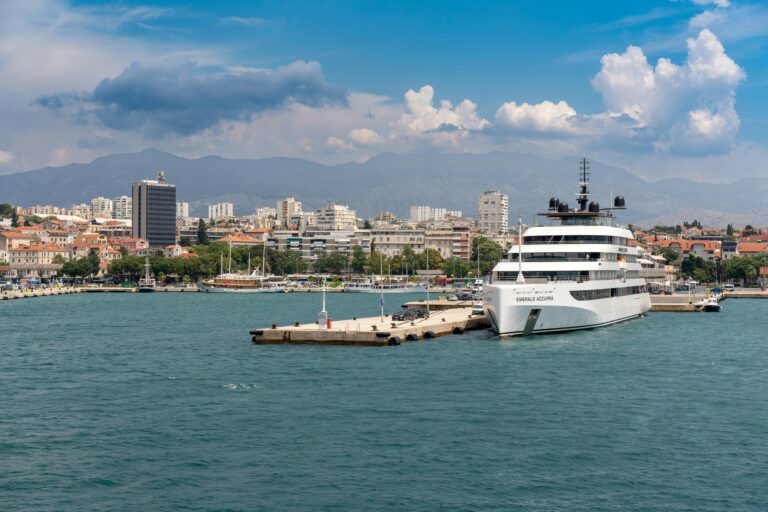 Ferry to Hvar (Starigrad) – Tips for a Hassle-Free Departure from Split 1 A luxury yacht anchored in Split harbor with cityscape and mountains in the background under a clear sky.